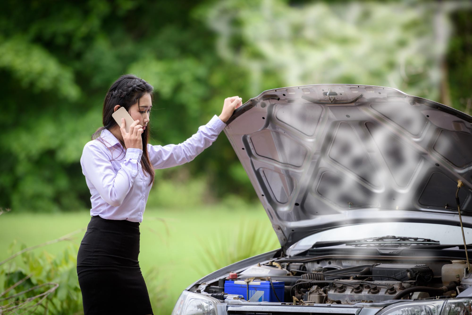 Autofahrerin telefoniert bei Panne – typische Symptome und Anzeichen eines Motorschadens erkennen.
