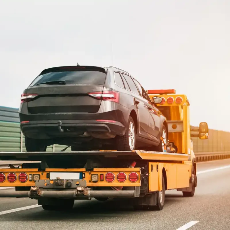 Gelber Abschleppwagen transportiert defekten Kombi auf der Autobahn Autoguru24/7 holt Ihr Auto mit Schaden deutschlandweit kostenlos ab.